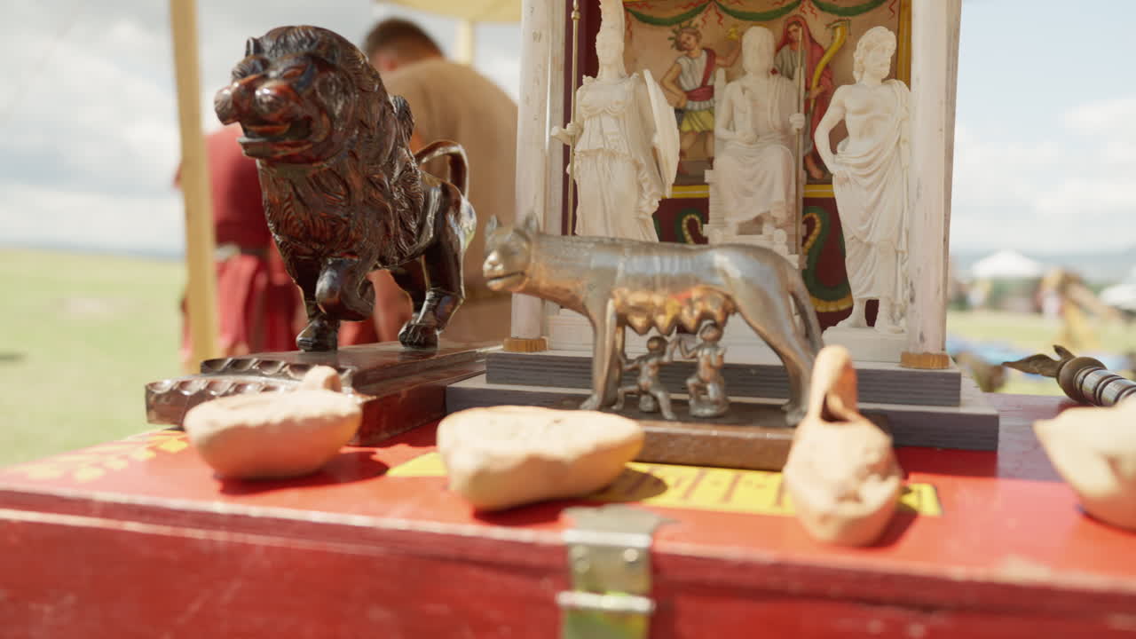 A slow dolly shot moves past a display of ancient Roman religious artifacts. The collection includes a replica of the Capitoline Wolf, a shrine to the gods, and other figurines