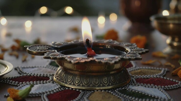 Burning brass diya oozing red wax on balcony, breeze causing flicker during offering with marigold