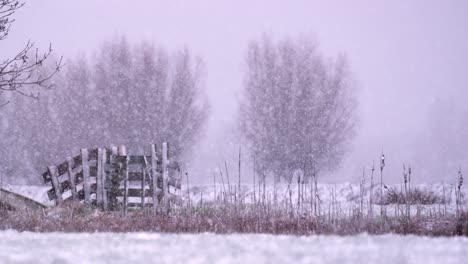 beautiful static show of heavy snow fall on part of an old wooden fence in the middle of a field, slow motion