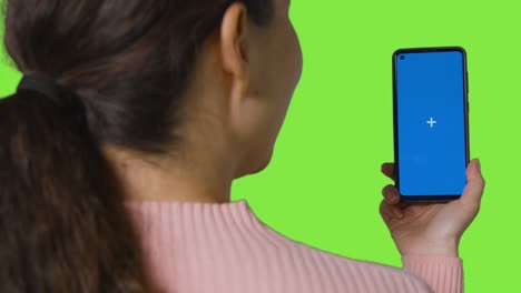 vista trasera de la mujer haciendo una llamada de video en la pantalla azul del teléfono móvil contra la pantalla verde