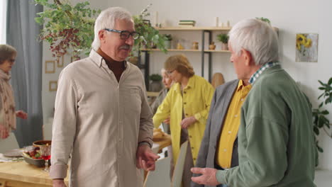 senior men speaking while women setting dinner table