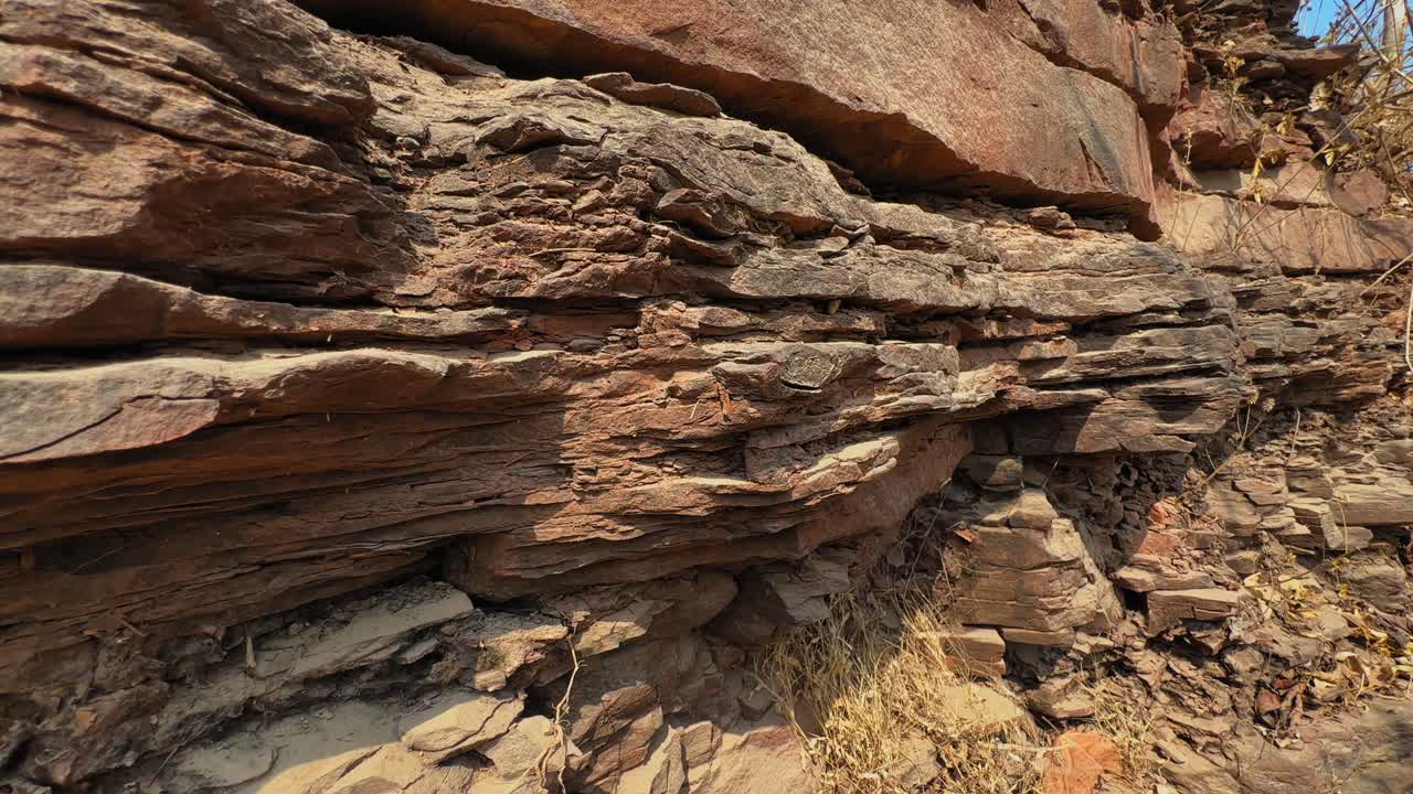 Följeslagning längs exponerade sedimentära berglager på en bergssluttning som avslöjar horisontella skikt, vittrade texturer och naturliga geologiska formationer.