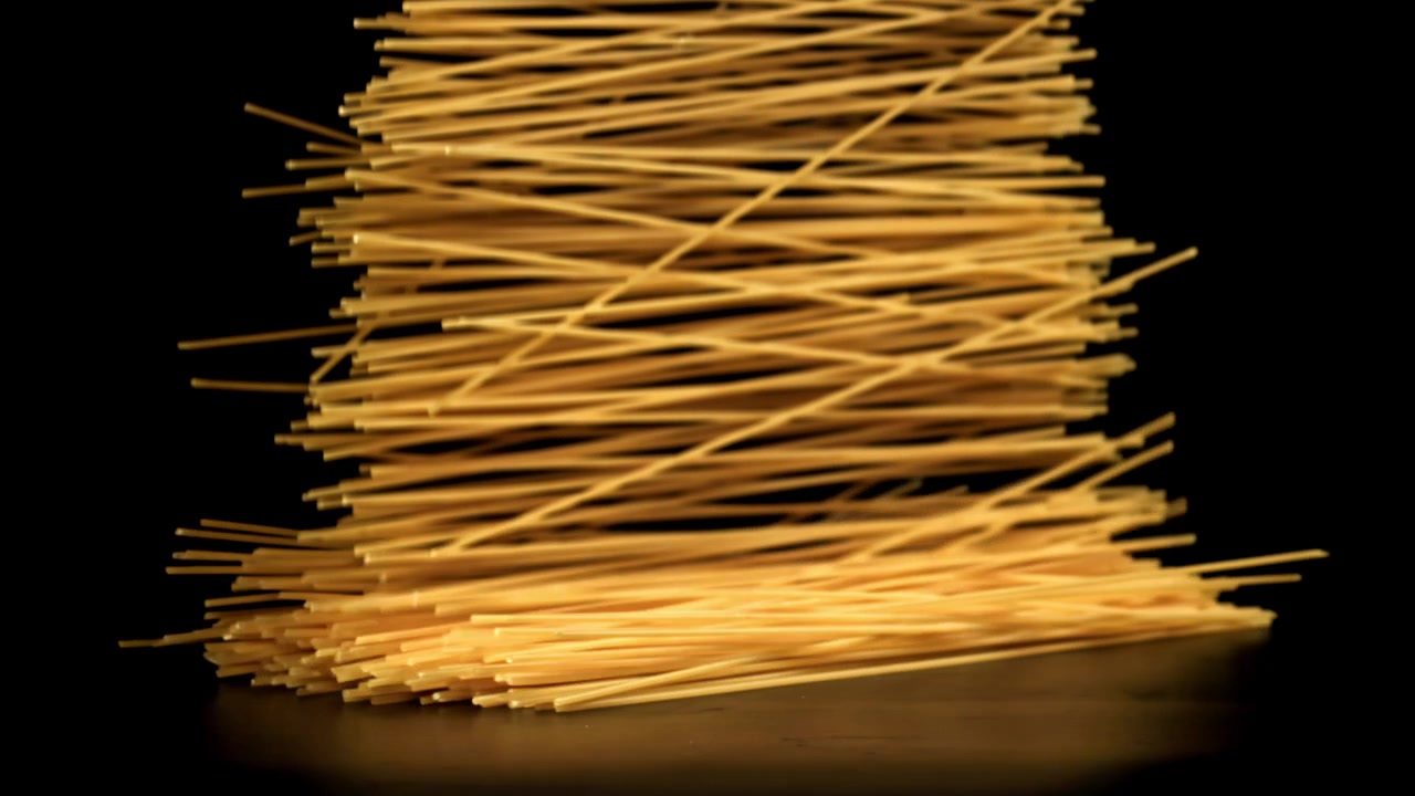Spaghetti secchi che cadono al rallentatore su sfondo nero