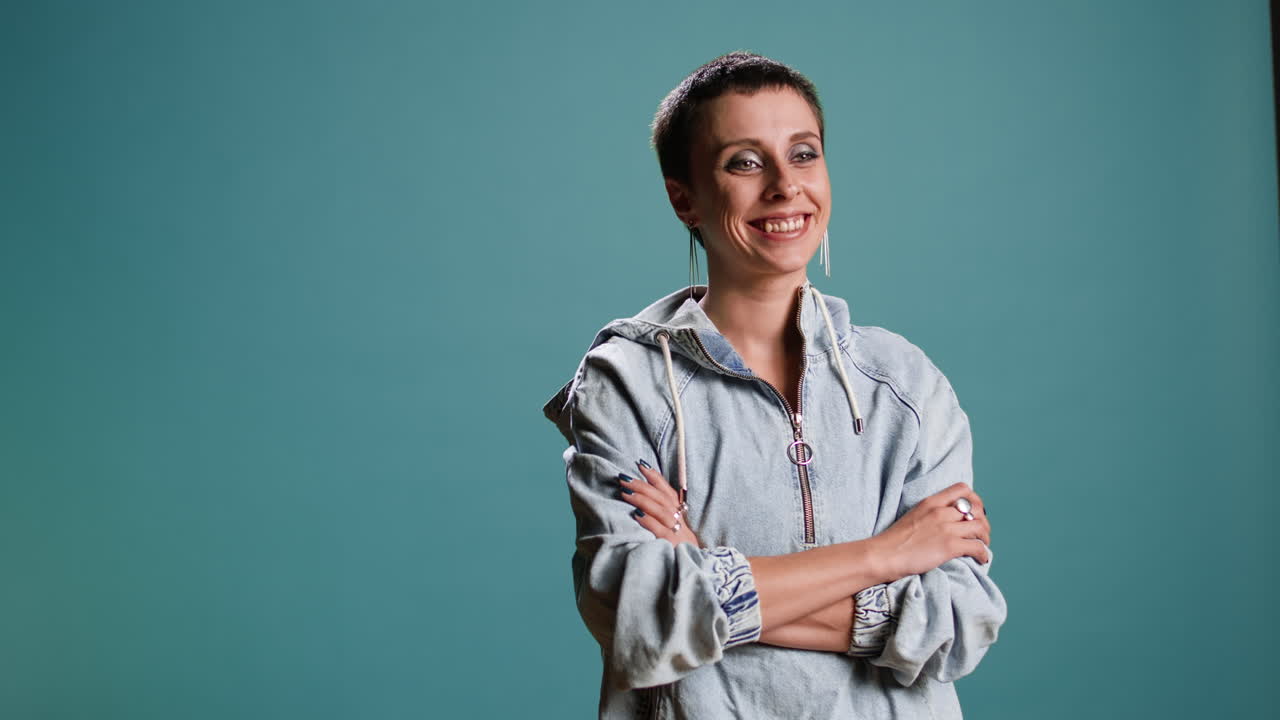 Woman in a hoodie with arms crossed on a turquoise background