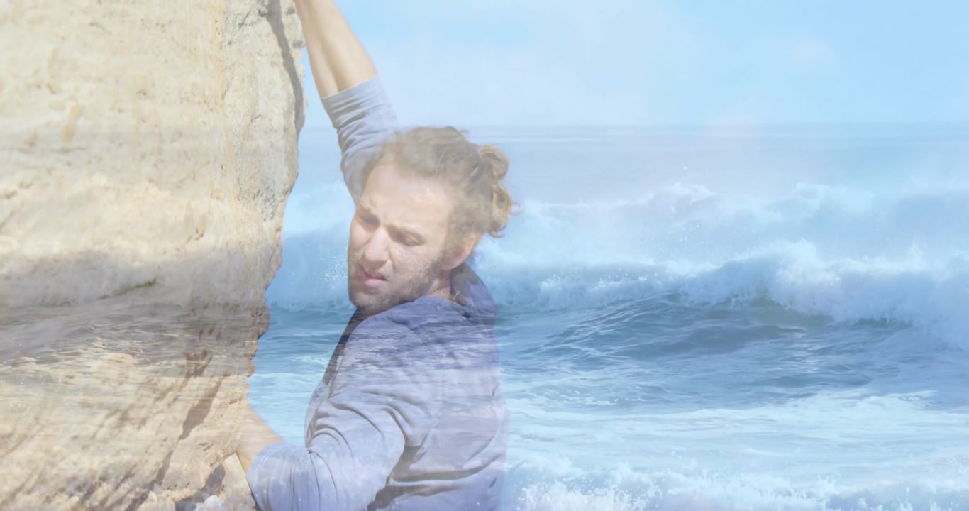 Climber placing hands on ledge and scanning holds, ascending cliff for fitness beside ocean waves