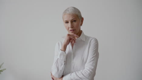 intrigued elderly woman thinking with hand on chin while looking at camera on white background