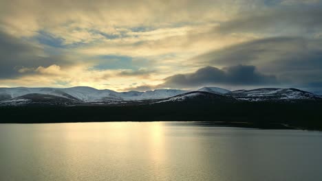 Looking-across-a-picturesque-lake-towards-a-sunset-over-snow-capped-mountains