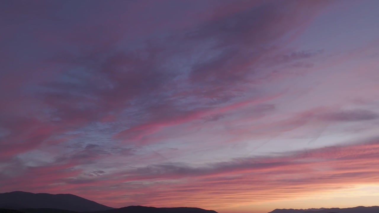 Panoramica drone verso destra che cattura uno spettacolare cielo al tramonto sopra la Valle del Tiétar, dove la luce del sole filtra dietro le cime della Cordigliera Centrale, creando colori vivaci e nuvole drammatiche.