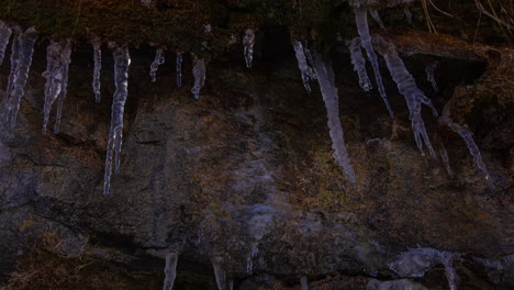 Eiszapfen-An-Der-Seite-Einer-Sandsteinklippe-Schmelzen,-Tropfen-Und-Gefrieren-Wieder,-Während-Schatten-Die-Bewegung-Der-Sonne-Anzeigen-–-Zeitraffer