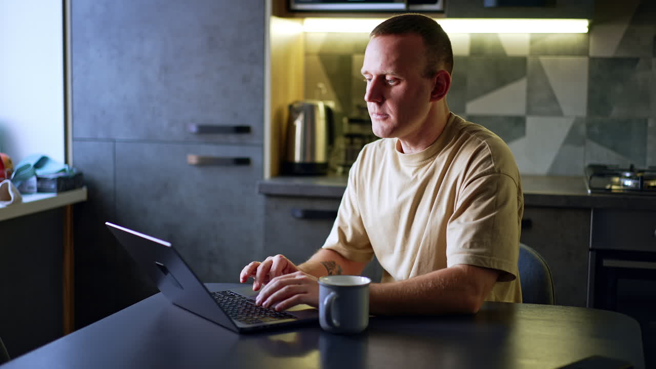 Thoughtful man sits looking at laptop screen. Portrait of a man working from home.