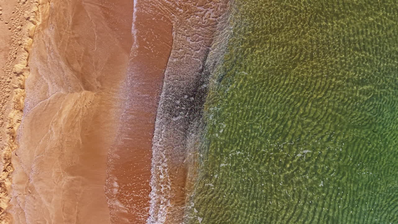 Waves gently kiss sandy shores, creating a serene landscape of blending colors and textures at the seascape's edge