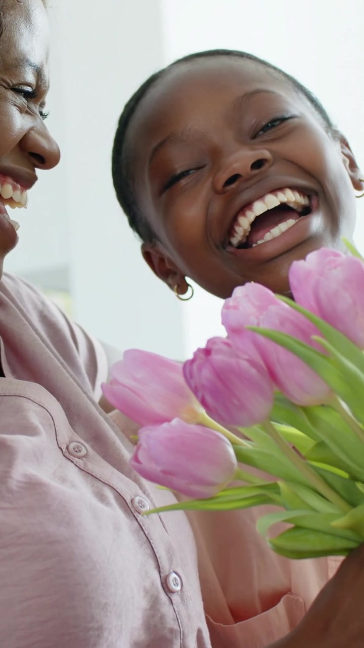 Vertical video: Mother giving pink tulips, daughter pale pink grabbing flowers celebrating at home