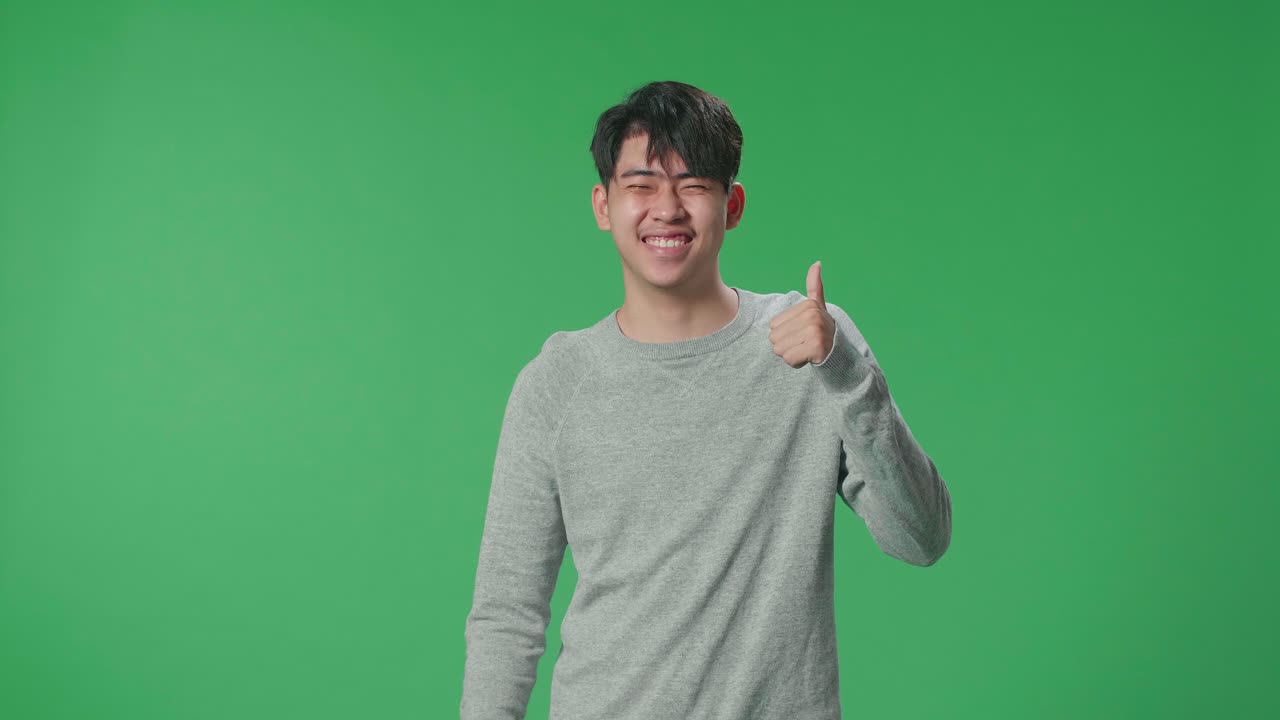 An Asian Man Showing Thumbs Up Gesture And Smiling While Standing In The Green Screen Studio