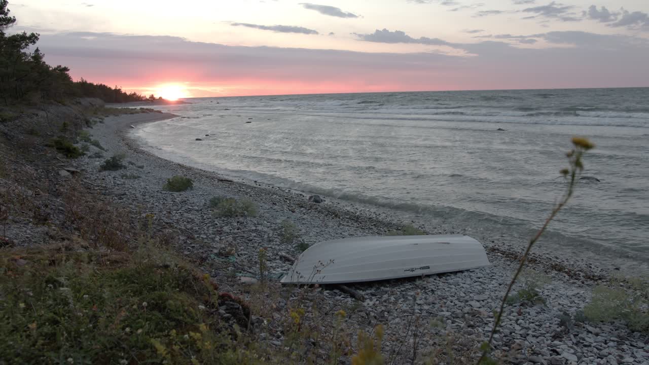Baltic seashore during sunset, waves hitting the rocky beach with a small rowboat in the bottom of the frame