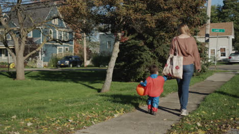 a woman leads by the hand a little boy in a costume, they go for candy on halloween