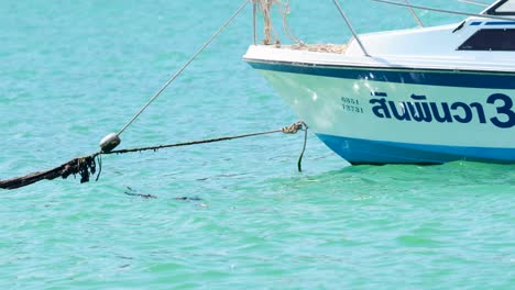 a boat remains anchored in the turquoise waters of phuket, thailand, gently swaying with the waves under bright daylight