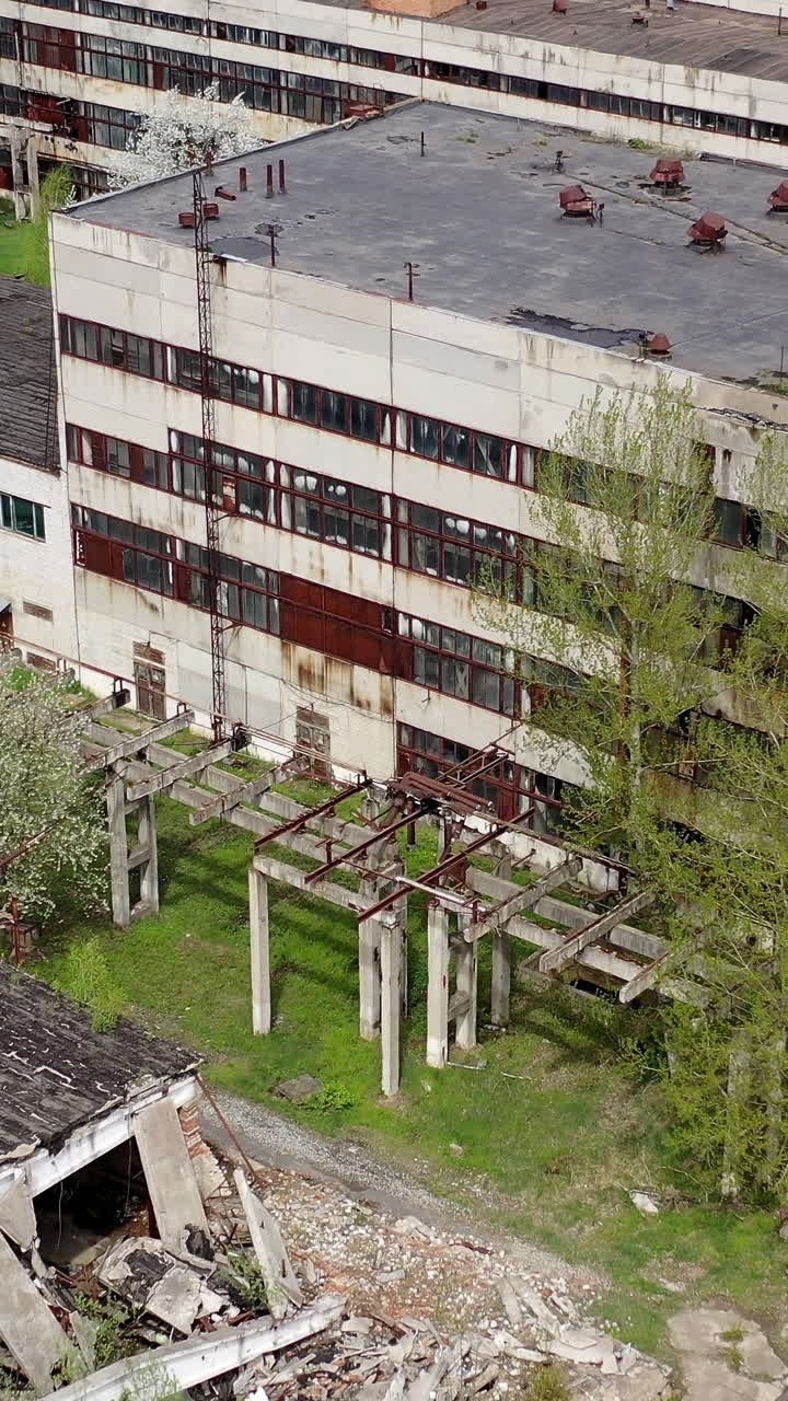 Damaged ancient factory. Broken industrial old plant in springtime. Abandoned place with ruined buildings. Aerial view. Vertical video