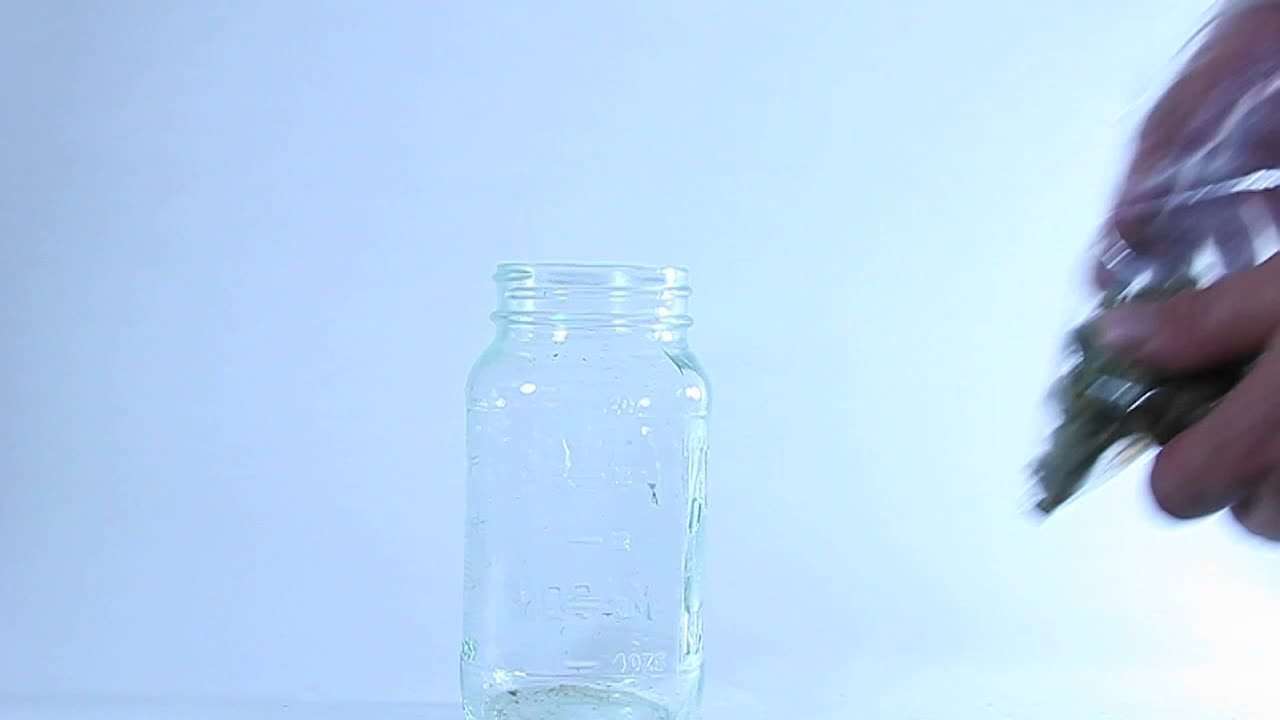 Hands transfer marijuana from a plastic bag to a glass jar