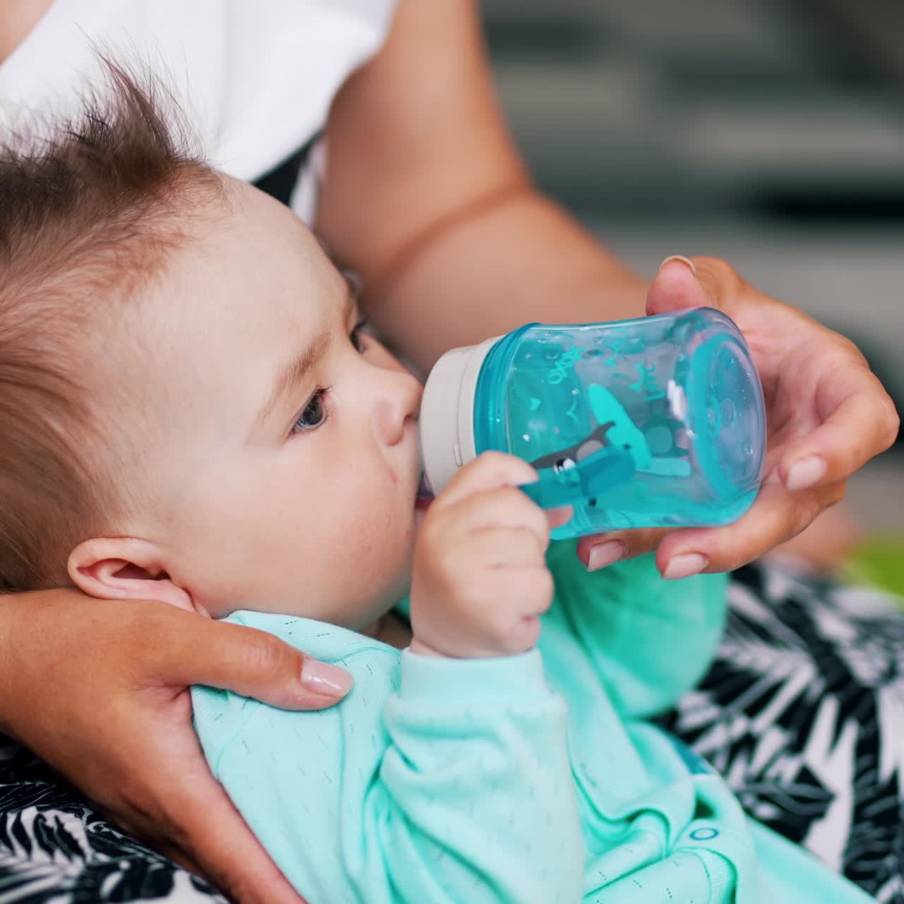 Mommy is giving a bottle with water for her baby. Cute child doesn't want to let go the bottle. Close up
