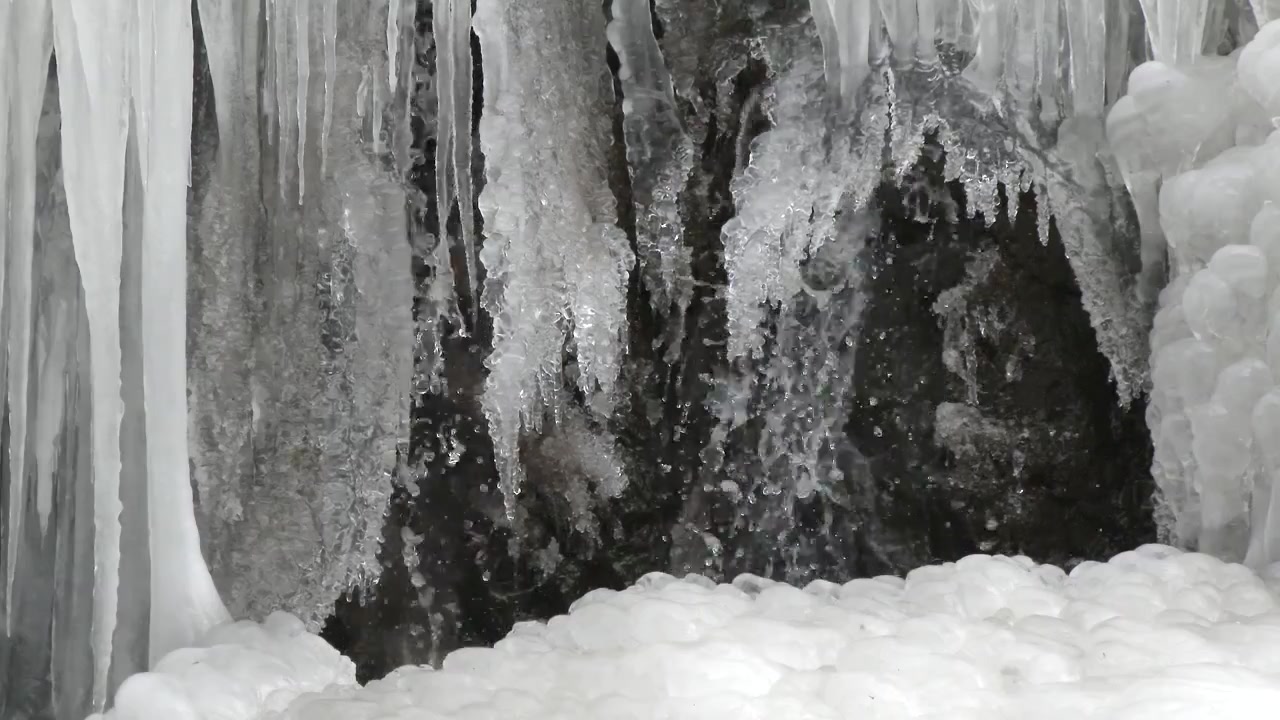 Água fluindo sobre rochas congeladas e pingentes de gelo no inverno