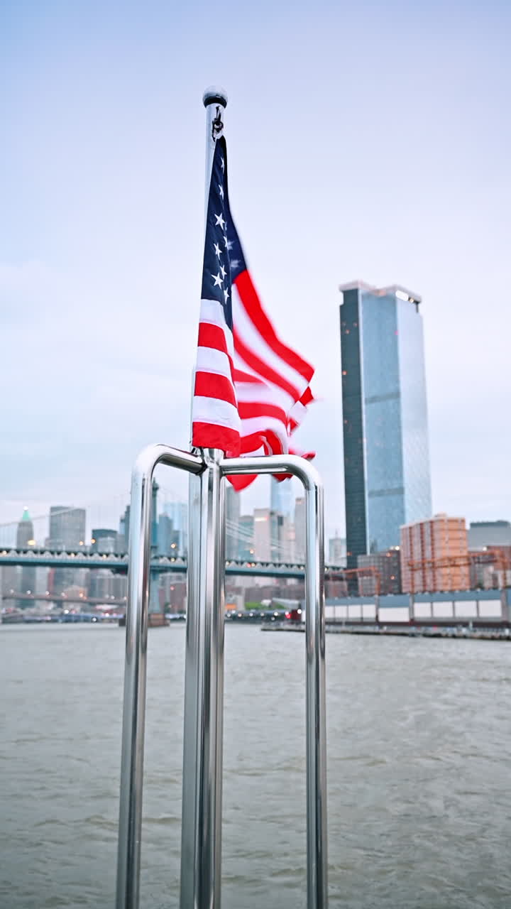 Bandiera sventolante vicino allo skyline di New York. La bandiera sventola in cima a una barca con lo skyline di New York che risplende nella luce serale dall'altra parte del fiume