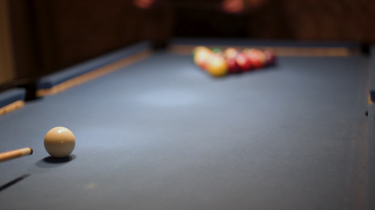 Player breaks billiard balls on indoor pool table, low lighting, shallow depth of field