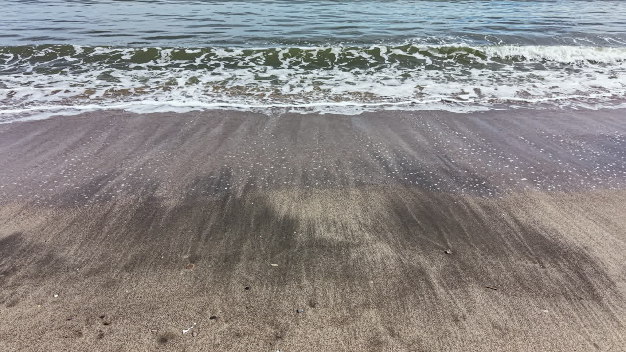 Bølger ruller ind på en sandstrand i dagtimerne med klar himmel og mildt sollys