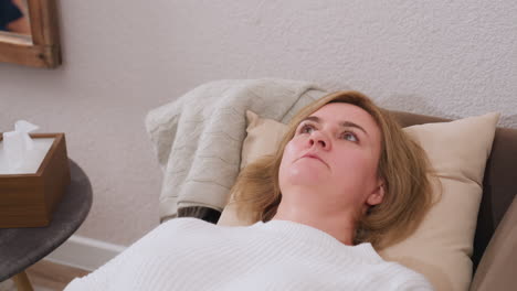 mindful partner lies on comfortable sofa facing upward conversing with counselor, pillows support head, table nearby holds clock, tissue box and pencils, carpet, warm therapy setting