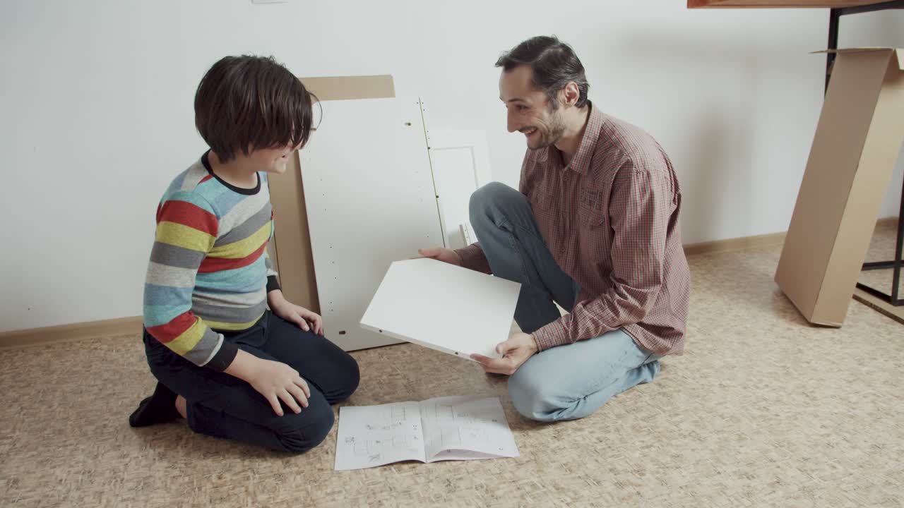 imágenes emocionales positivas. padre e hijo se comunican alegremente y ensamblan muebles de acuerdo con las instrucciones en el suelo de la habitación. ayuda con la tarea