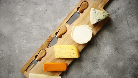 assortment of various kinds of cheeses served on wooden board with fork and knives