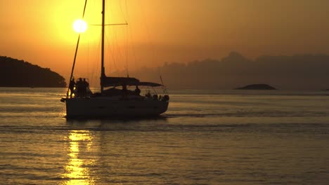 sunset at vela luka, croatia, with a sailboat and motorboat crossing the view