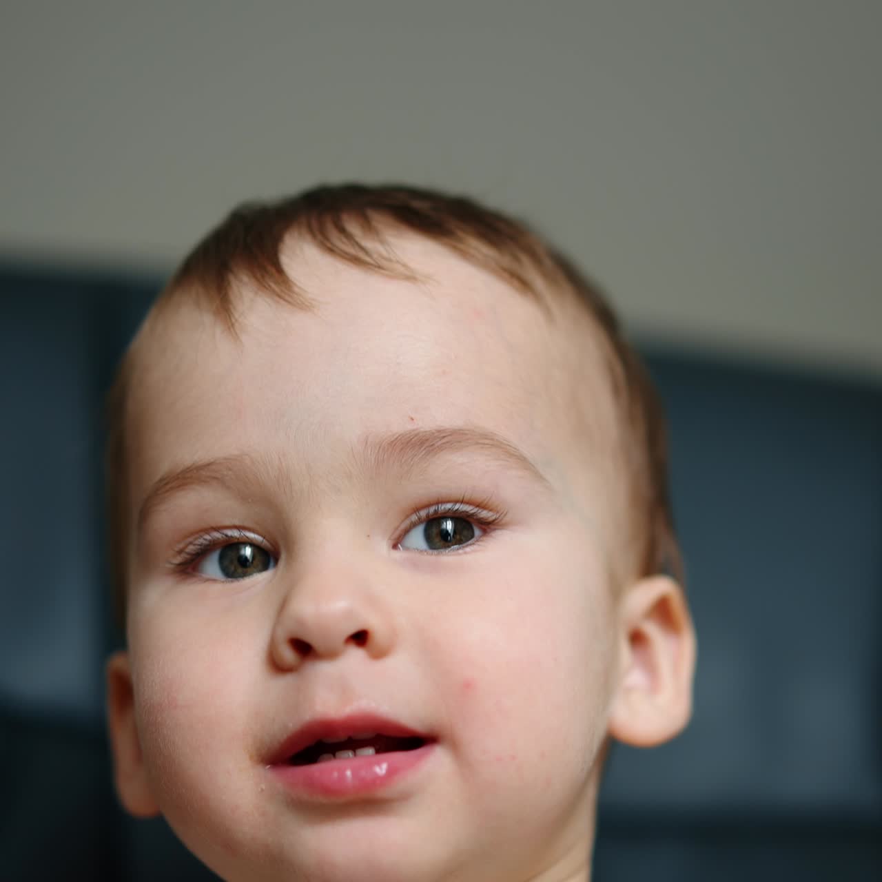 Beautiful joyful kid shows tongue to camera. Kid sits in black chair looking and speaking to camera. Close up
