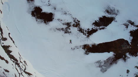 Aerial-ascending-shot-of-a-person-laying-in-the-snow-and-the-camera-shooting-up-revealing-a-mountain-peak-and-cliff-with-fog-and-mist