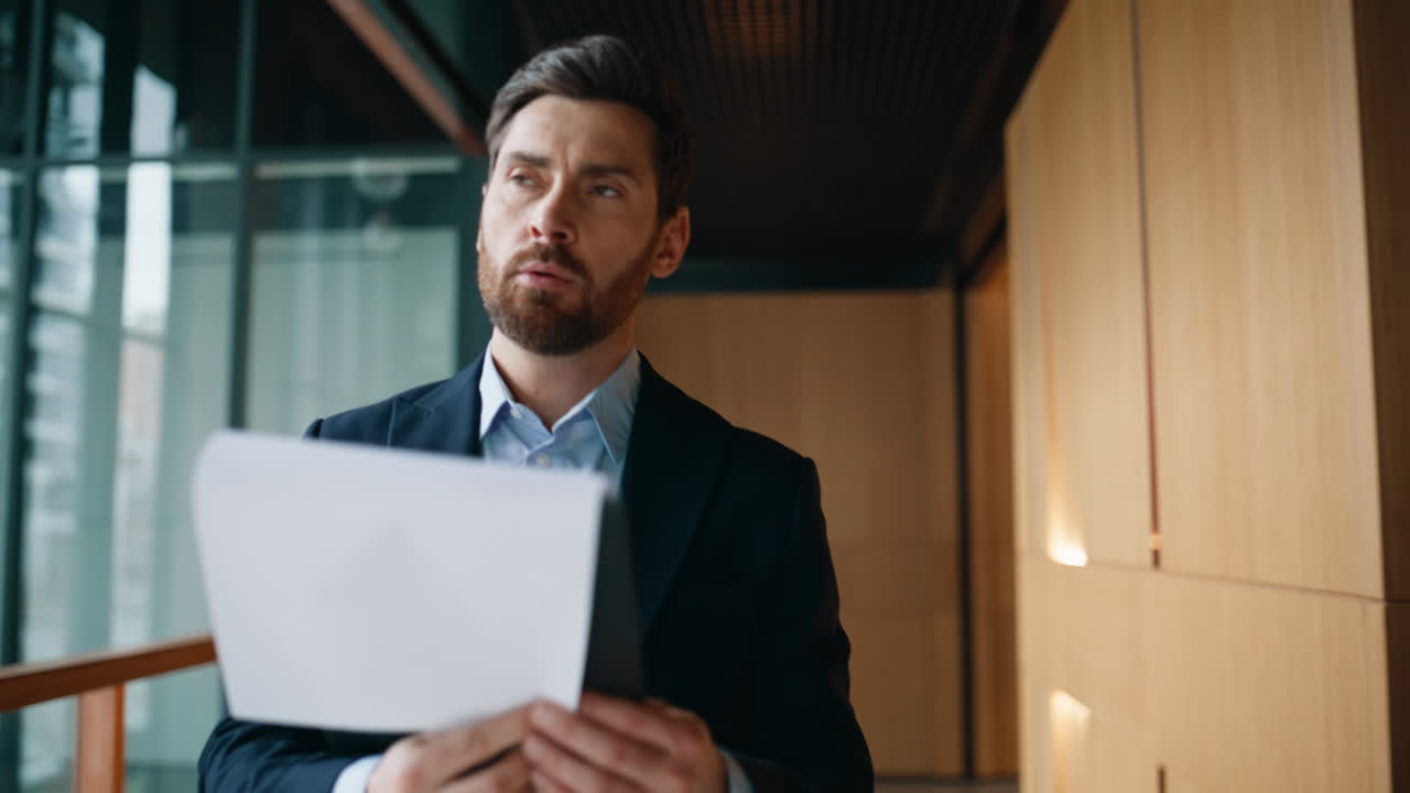 Pensive entrepreneur reviewing papers walking modern company hallway closeup