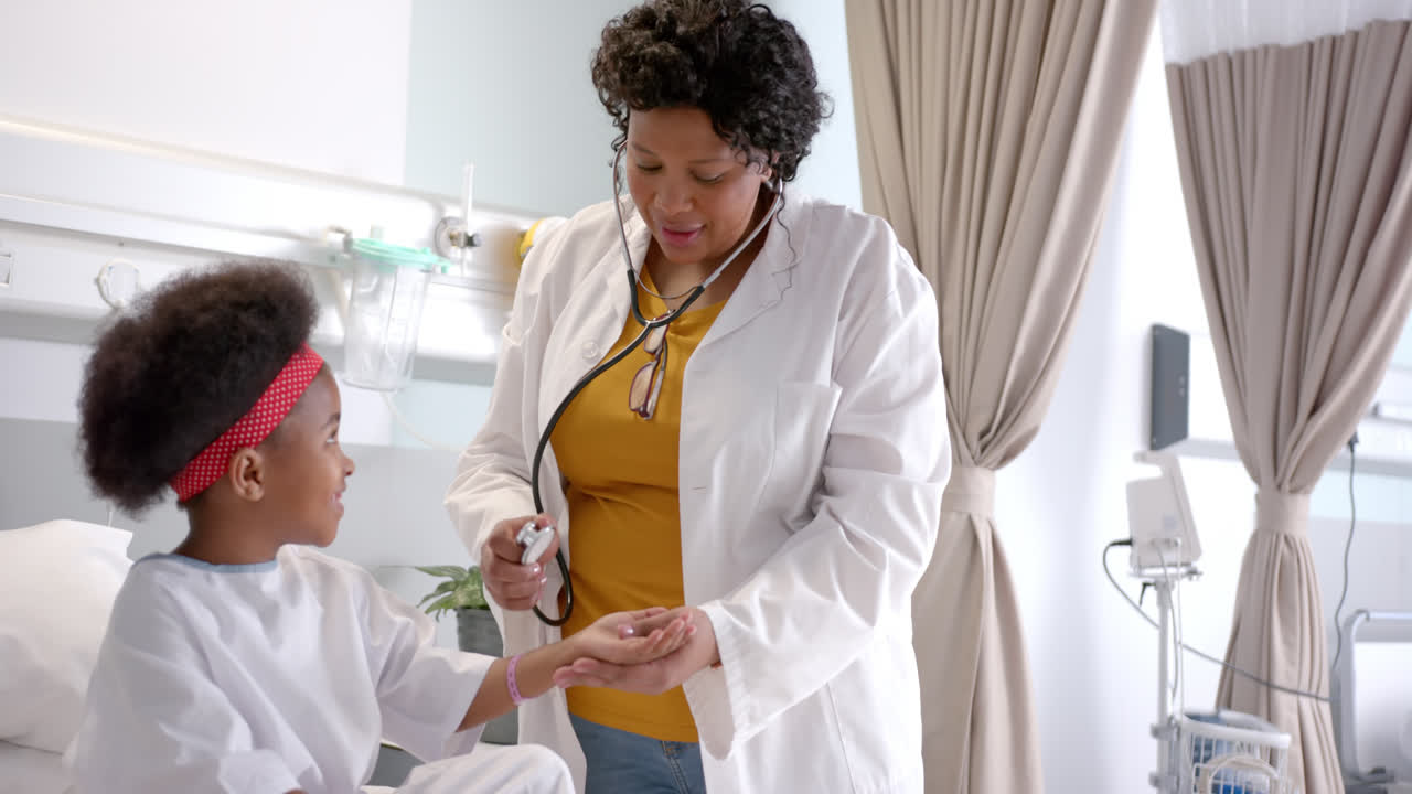 African american female doctor examining girl using stethoscope in hospital room, slow motion