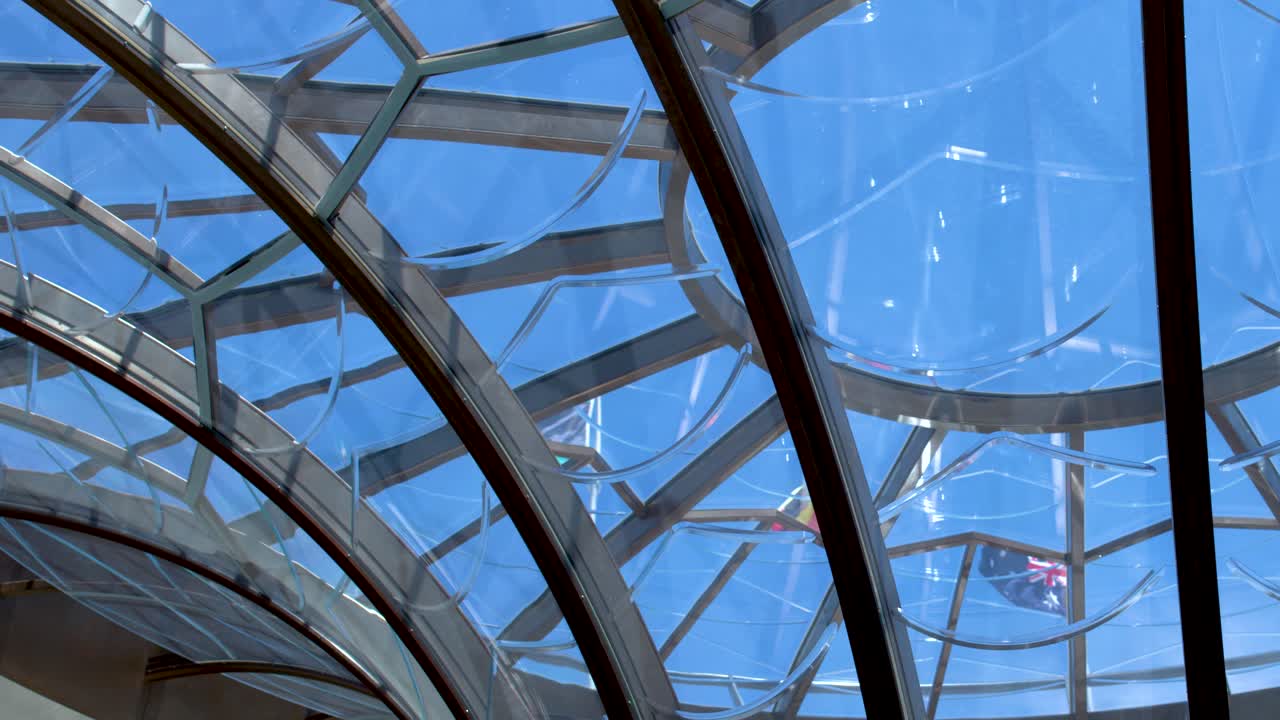 Low angle shot of a geometric glass ceiling dome with blue sky visible through framework