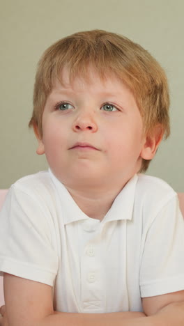 cute toddler boy listens to teacher with folded hands on desk. kid licks lips looking at blackboard in classroom slow motion. educational process