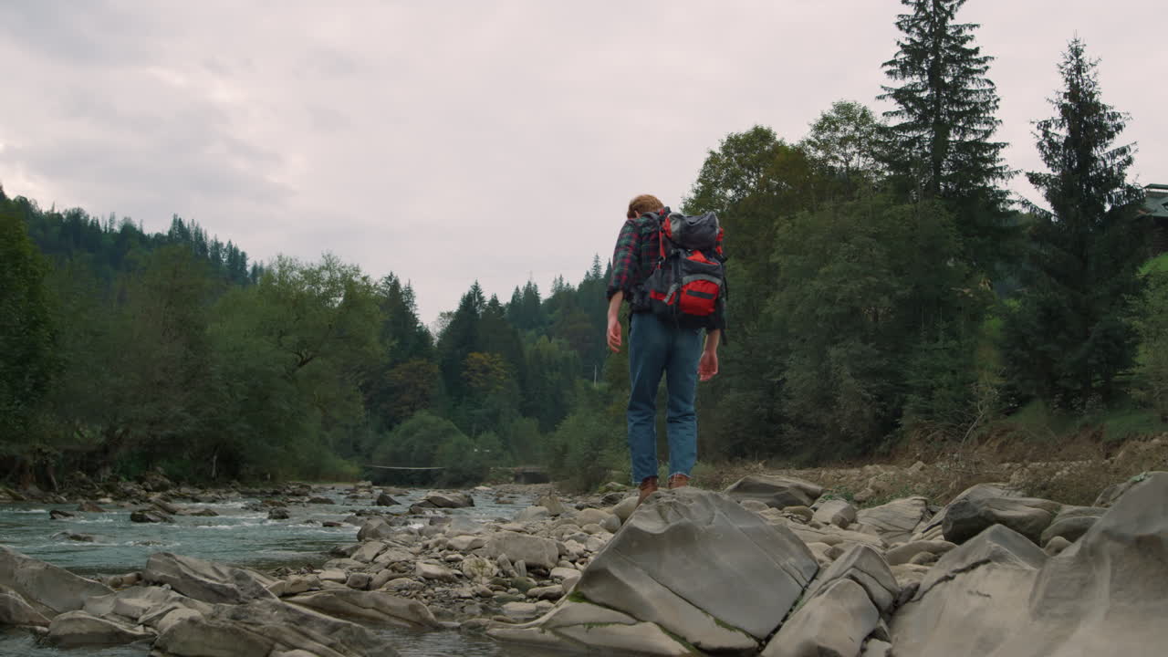 hombre caminando sobre rocas en el río. turista masculino caminando a lo largo del río en el bosque