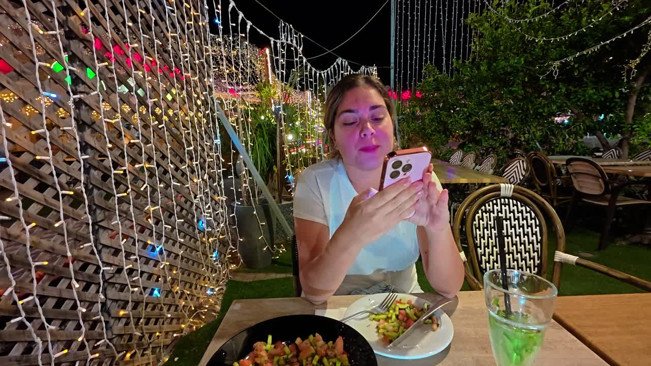 Woman Smiling at Her Phone While Eating Dinner Alone