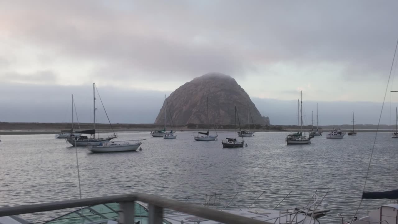 Gimbal wide dolly shot of sailboats in Morro Bay with Morro Rock in the distance on the Central Coast of California. 4K