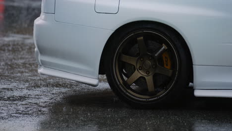 the white car with its wheels spins as the rain pours down