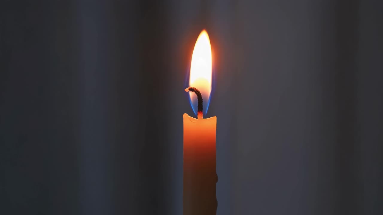 Vidéo en gros plan d’une flamme de bougie unique sur un arrière-plan sombre, filmée en angle droit