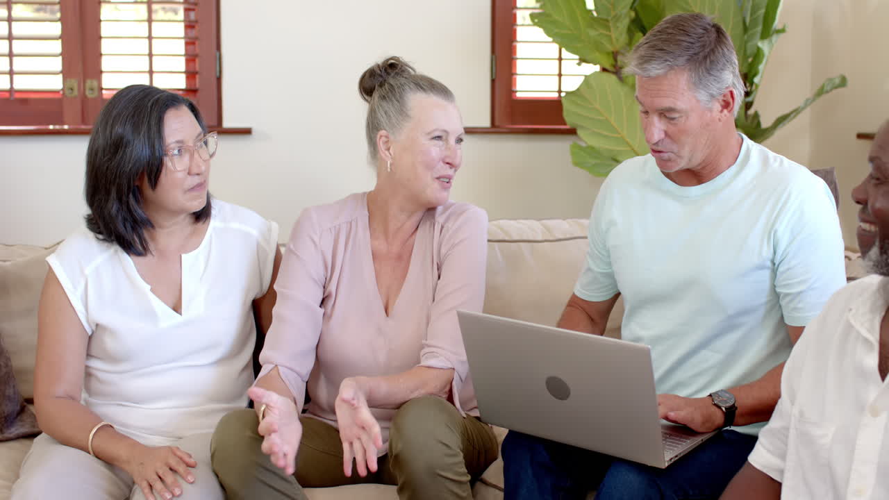 Senior group discussing project while using laptop, smiling and engaged at home