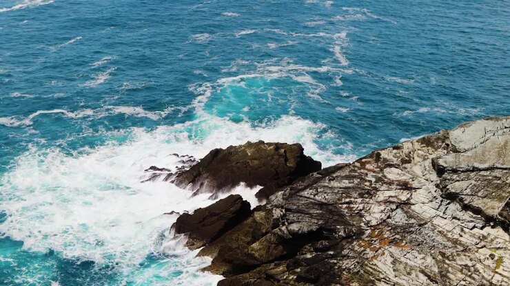 Piccole onde atlantiche che si infrangono contro una costa rocciosa in una giornata di sole.