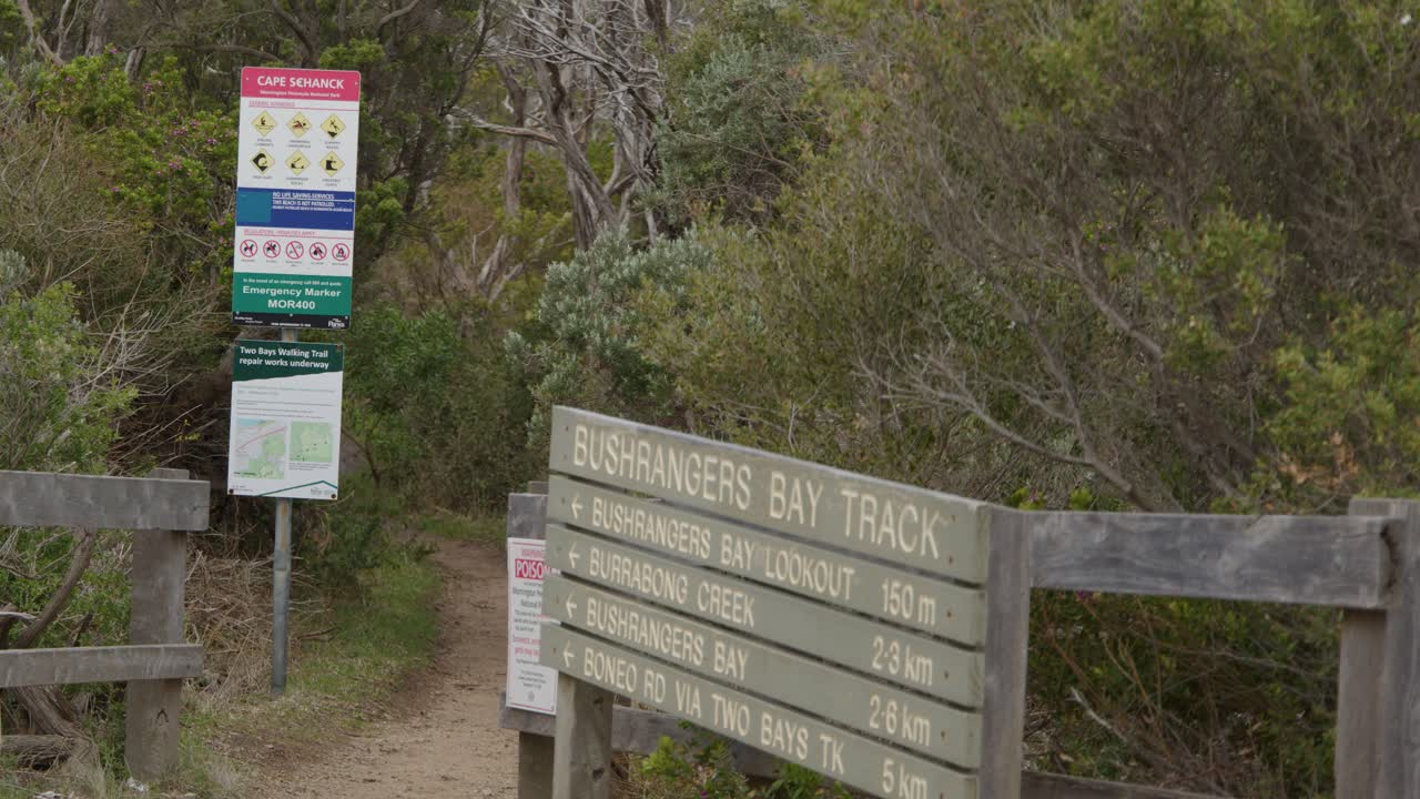 Camera slowly moves toward trailhead sign and information board, overcast daylight, natural bushland setting