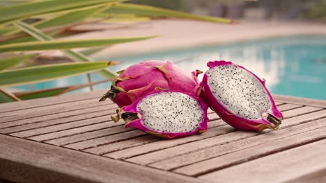 zoom in of sliced dragon fruit on wooden table with swimming pool in the background at sunset