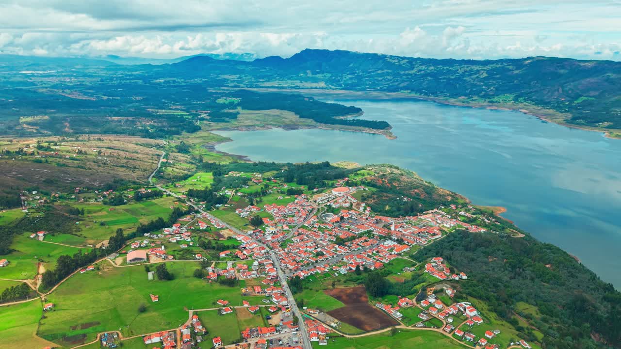 Scenic wide shot of Guatavita, Colombia, showing Tominé Reservoir, red roofs, and lush green nature.