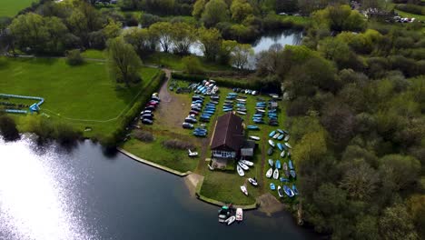 aerial dolly view of a boatyard beside a shelter house surrounded by lush green fields and deep forests in uk