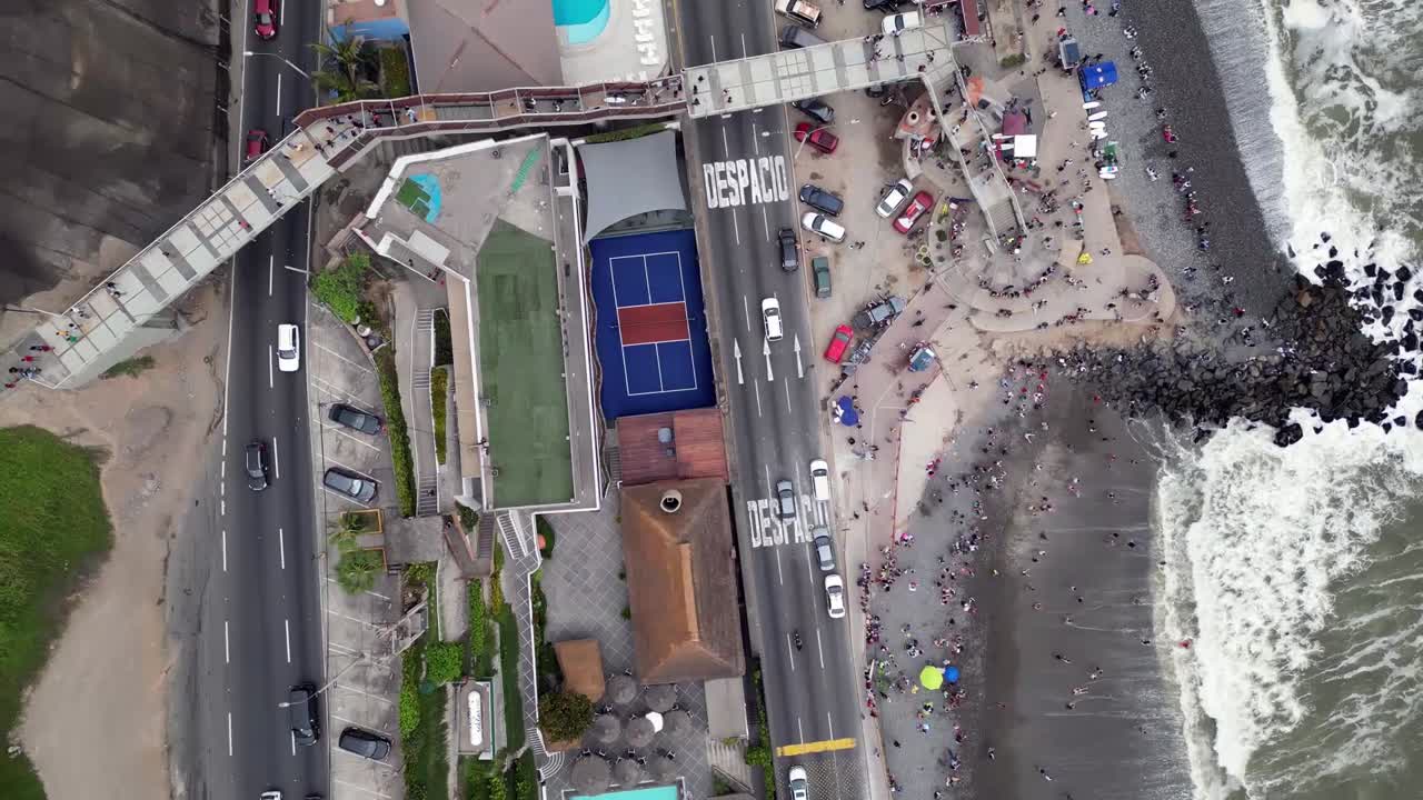 다음 자동차  ⁇ 은 남미 해안 거리를 보여줍니다. 비어있는 해변 클럽과 바다 사이에 사람들이 수영하고 서핑 보드를하고 있습니다.