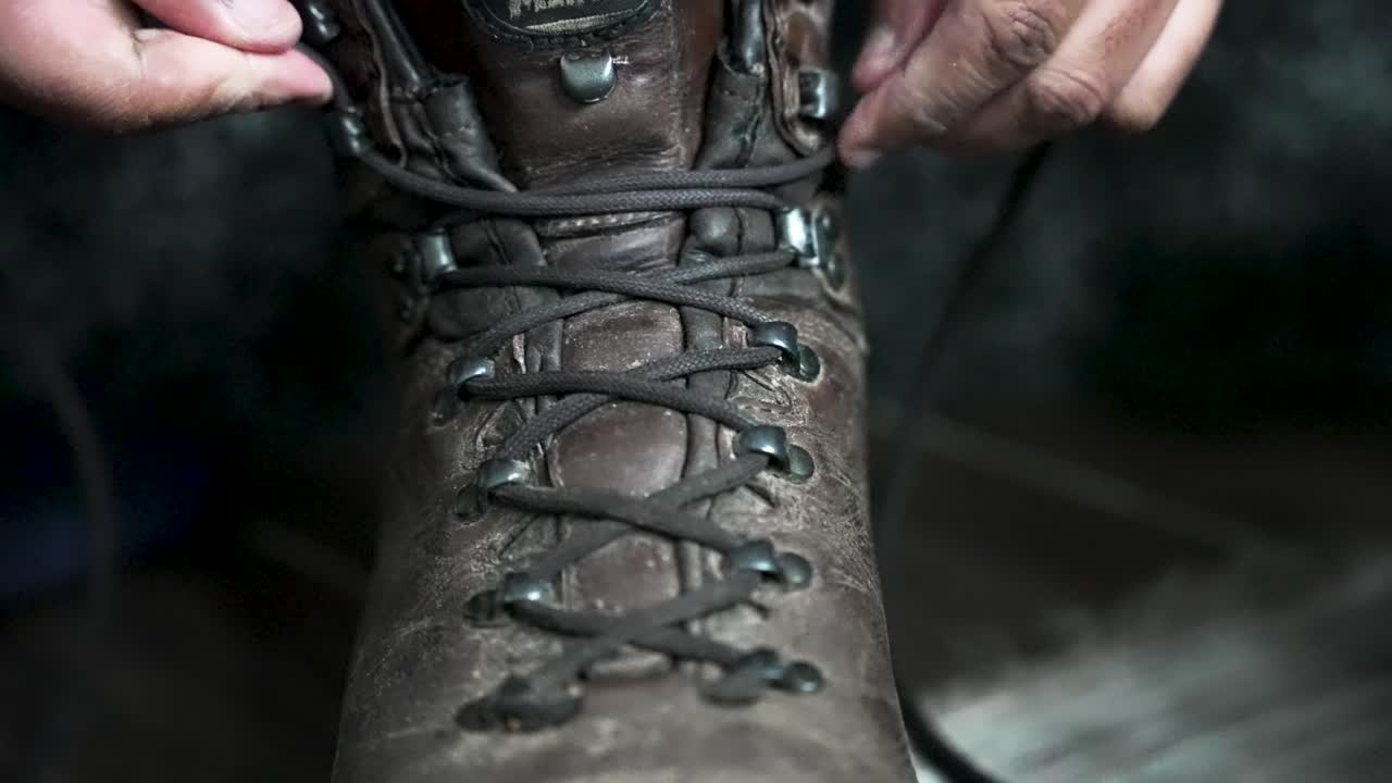 Close-up tangan mengikat tali sepatu bot hiking kulit berwarna cokelat, menyampaikan daya tahan yang kuat dan kesiapan untuk aktivitas luar ruangan